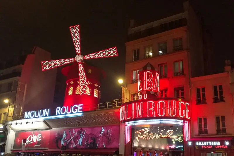 Façade du Moulin Rouge illuminée en rouge la nuit, avec son moulin et ses enseignes au néon