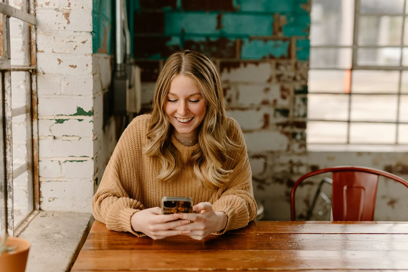 Jeune femme souriant en lisant un message sur son téléphone dans un café
