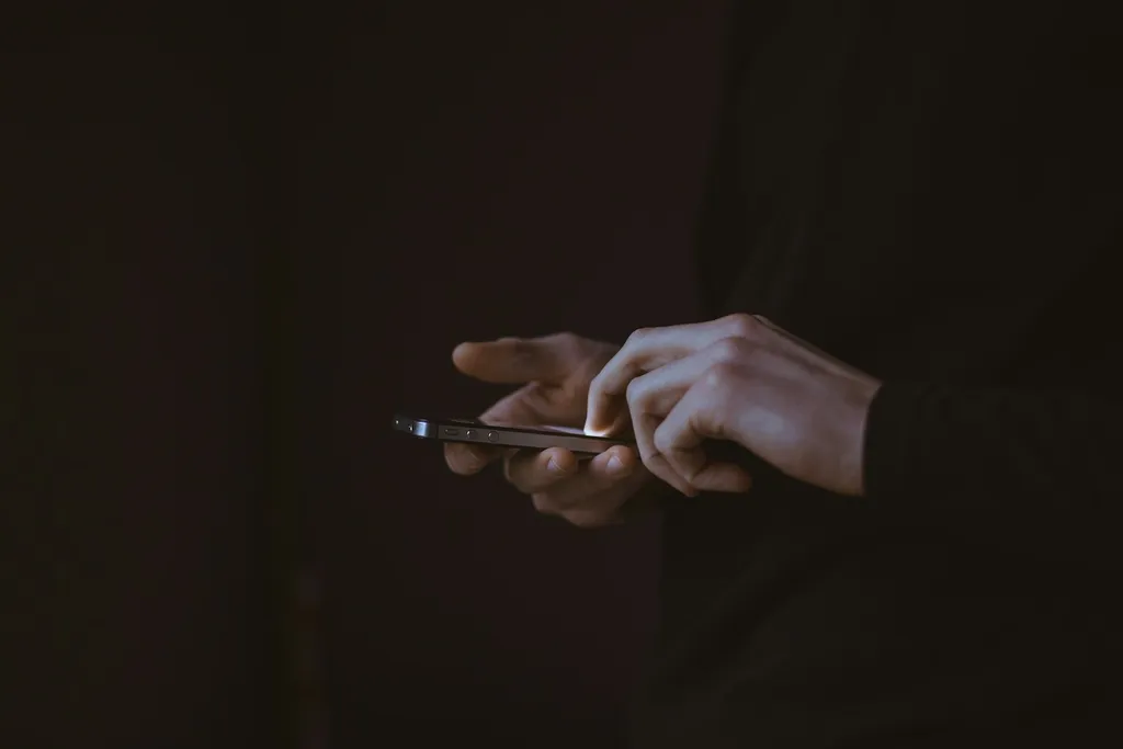 Mains composant un premier message sur un smartphone dans la pénombre