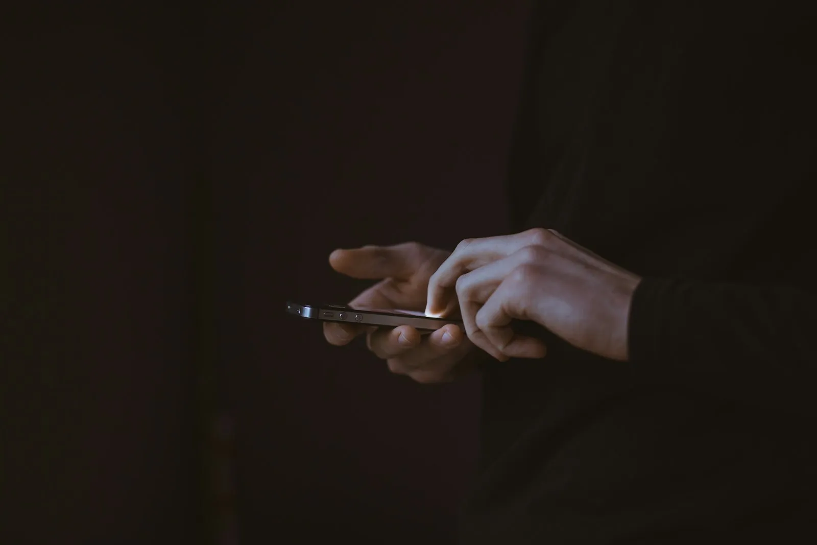 Mains composant un premier message sur un smartphone dans la pénombre