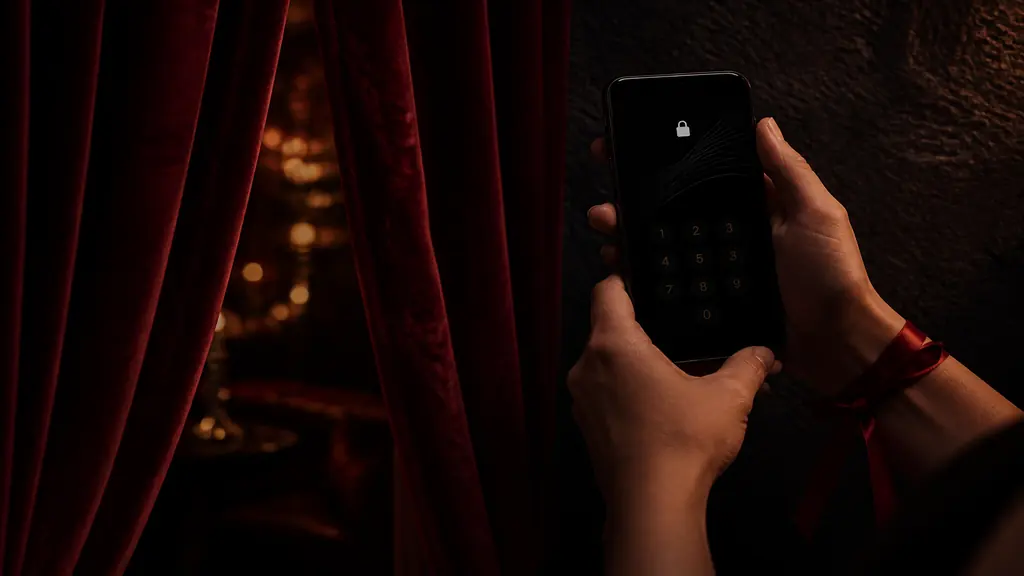 Mains tenant un smartphone avec écran de verrouillage devant des rideaux de velours rouge entrouverts