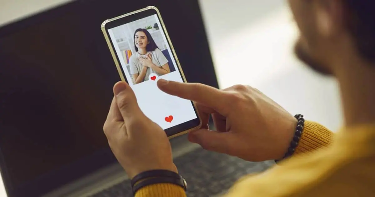Main tenant un smartphone affichant le profil d'une application de rencontre, cœur rouge en surimpression