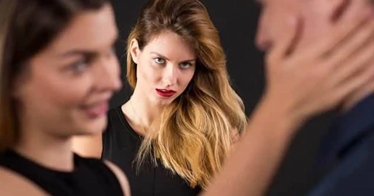 Une femme fixe la caméra pendant qu'au premier plan un homme et une autre femme se font face