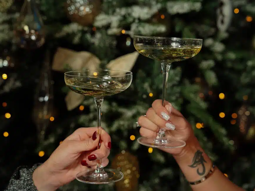 Deux mains trinquent avec des coupes de champagne devant un sapin de Noël décoré